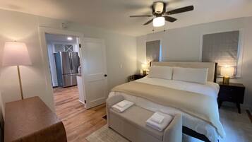 A hotel room with a bed, bedside tables, a ceiling fan, and a view into the kitchen.