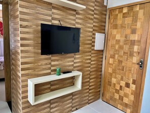 A room with a television mounted on a wooden wall, a white shelf below, and a wooden door. - 305 2 Bedrooms 15 min from the Center (Belém)