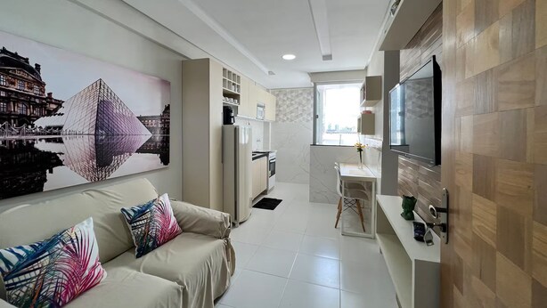A modern living room with a sofa, a TV mounted on the wall, and a kitchen area with a refrigerator and microwave. - 305 2 Bedrooms 15 min from the Center (Belém)