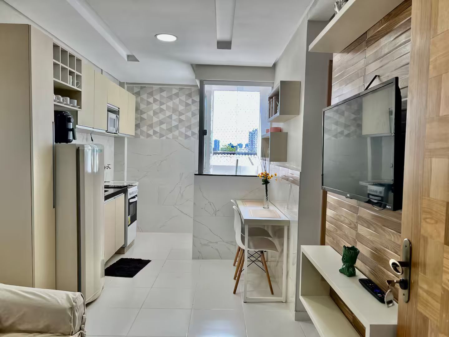 A compact kitchen with a built-in oven, a coffee machine, and a TV mounted on the wall.