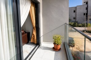 Un balcon avec une plante en pot, une porte coulissante et une vue sur un bâtiment en arrière-plan.