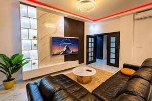 A modern living room with a black leather sofa, a round coffee table, a mounted TV, and a potted plant. - 2-bedroom apartment in awesome Dakar with AC and fitness room Fast Wifi (Dakar)