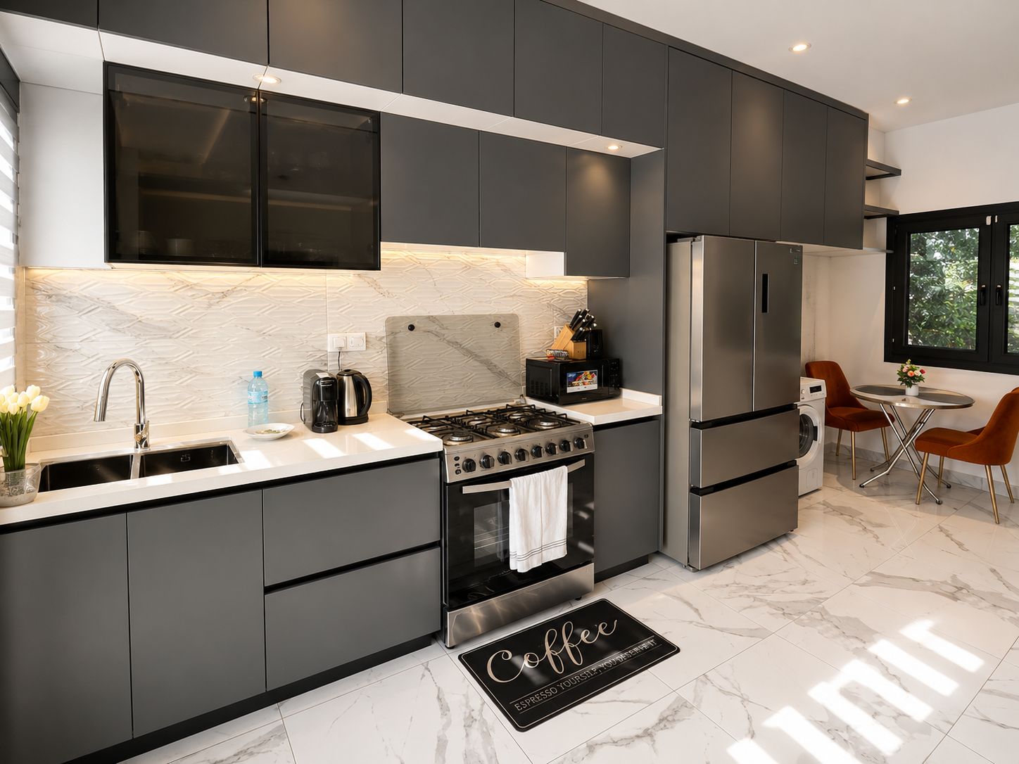 Una cocina moderna con armarios oscuros, un refrigerador de acero inoxidable, una estufa a gas y una cafetera.