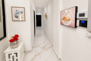 Un corridoio con pavimento in marmo, un vaso con fiori rossi e bianchi, un quadro incorniciato e un pannello di sicurezza a parete.