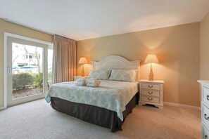 A bedroom with a bed, two bedside tables, a nightstand, a window with curtains, and a view of the outside. - Sun Drenched Villa With Pool and Tennis Access (Hilton Head Island)