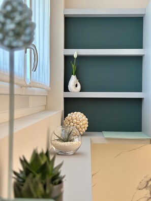 A room with a window, a white vase with a single flower, a glass bowl with a plant, and a decorative shell arrangement on a shelf. - Luxurious new apartment with a terrace overlooking the lake on the Sarnico lakeshore. (Sarnico)