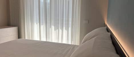 A hotel room with a bed, a bedside table, and a window with sheer curtains.