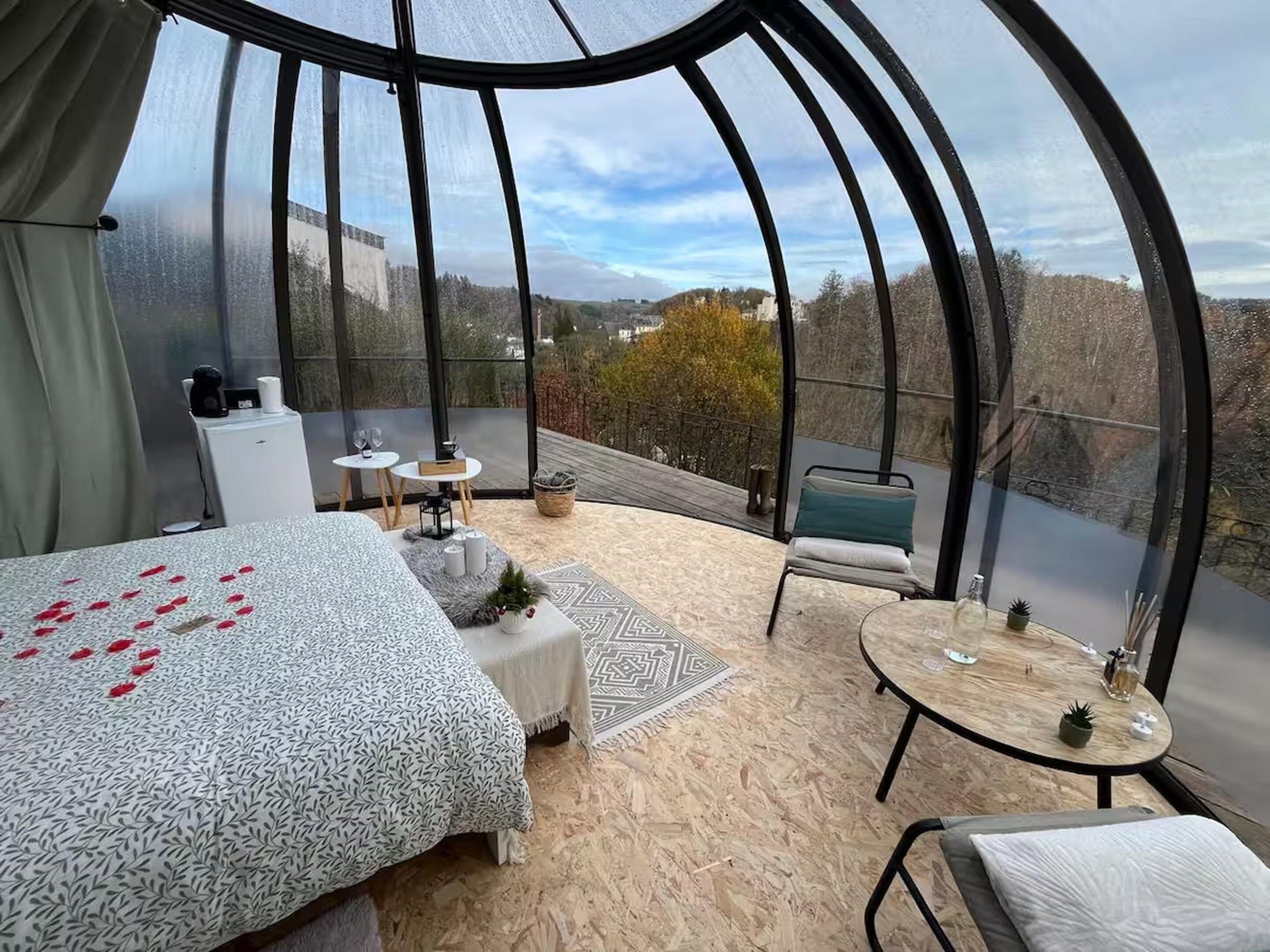A modern, enclosed room with a bed, seating area, and a table.