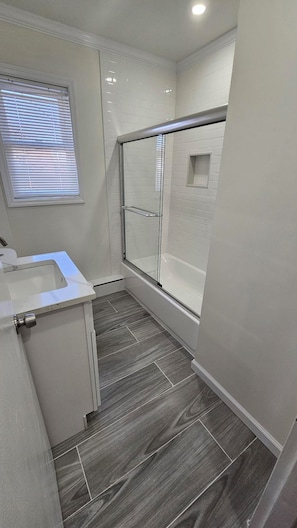 Uma casa de banho moderna com chuveiro em cabine de vidro, lavatório embutido e janela com persianas.