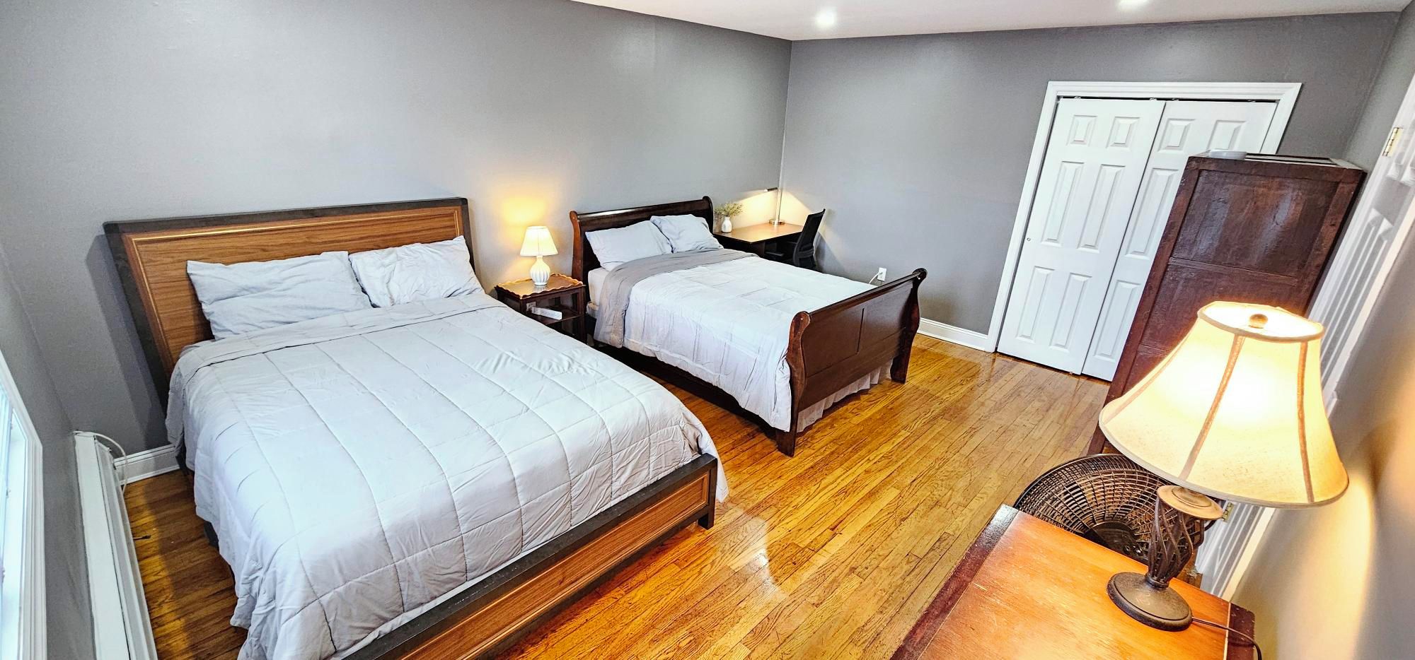A bedroom with two beds, a desk, a chair, and a lamp.