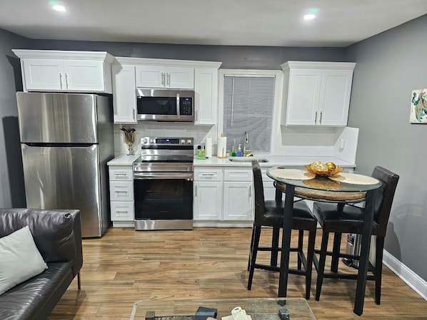 A modern kitchen with white cabinets, stainless steel appliances, and a dining area with a round table and chairs.
