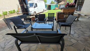 An outdoor patio with stone flooring, a white van, and a barbecue grill.
