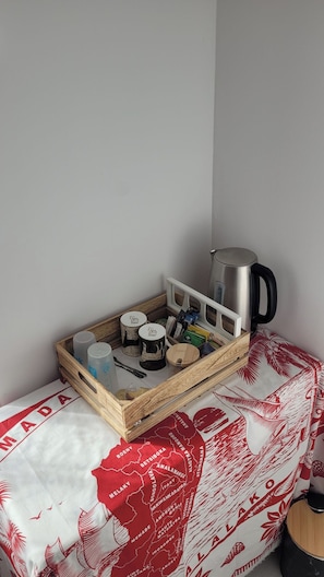 Una zona de cuina petita amb una cafetera, una safata amb tasses i pots, i un mapa sobre el llit.