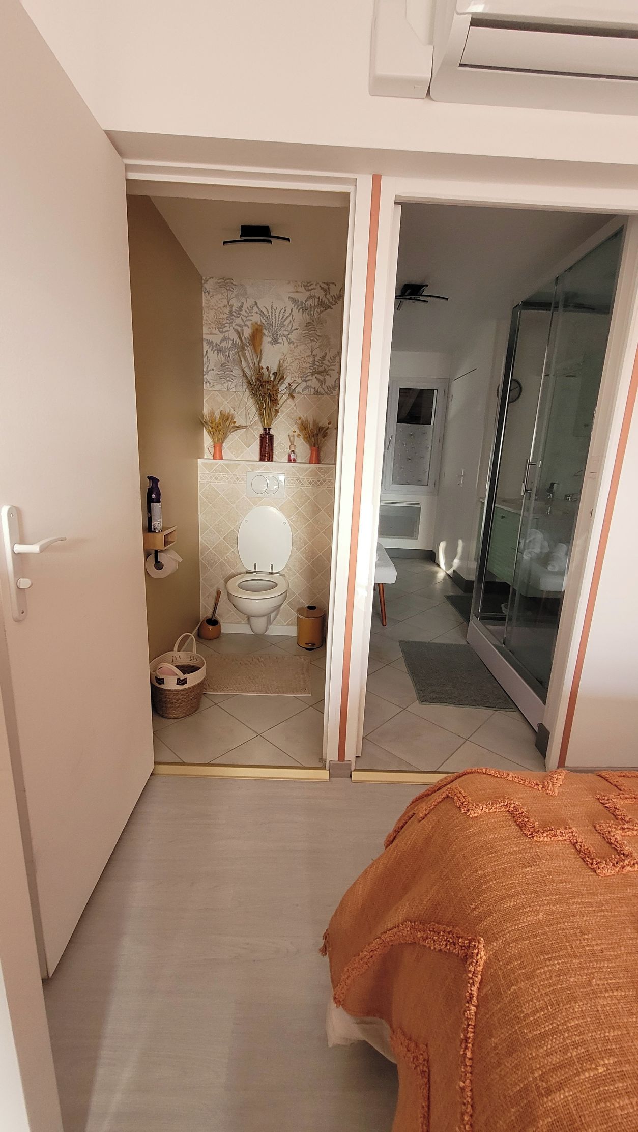 Une salle de bain comprenant des toilettes, une douche et une porte en verre donnant accès à l’espace douche.