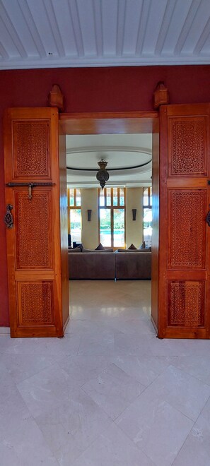 A doorway with intricate woodwork leading to a room with a sofa and a ceiling fan. - Villa Hana Marrakech, with views of the Atlas Mountains, nestled in a 1 ha park. (Sidi Abdellah Ghiat)