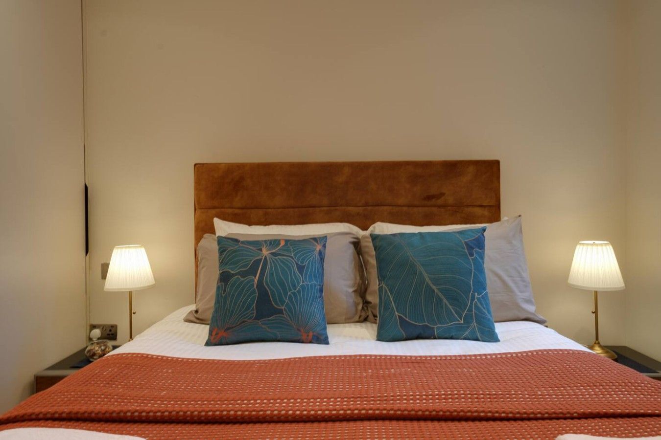 A hotel room with a bed, two bedside lamps, and a red blanket.