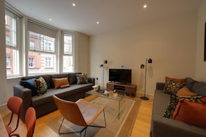 Ein modernes Wohnzimmer mit einer Couch, Sesseln, einem Couchtisch, einem Flachbildfernseher und Stehlampen.