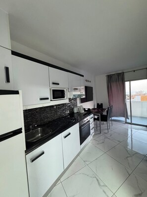 A modern kitchen with white cabinets, a black countertop, and a microwave. There is a dining area with a table and chairs. - Sea view modern apartment in Las Americas (Costa Adeje)