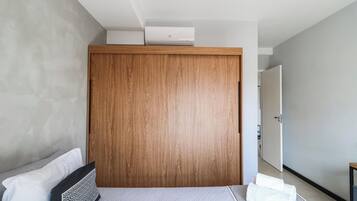 Quarto moderno com guarda-roupa de madeira, cama com colcha estampada e corredor que leva a uma porta.