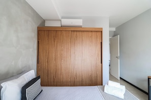 Un dormitori modern amb un armari de fusta, un llit amb un estovat estampat i un passadís que condueix a una porta.