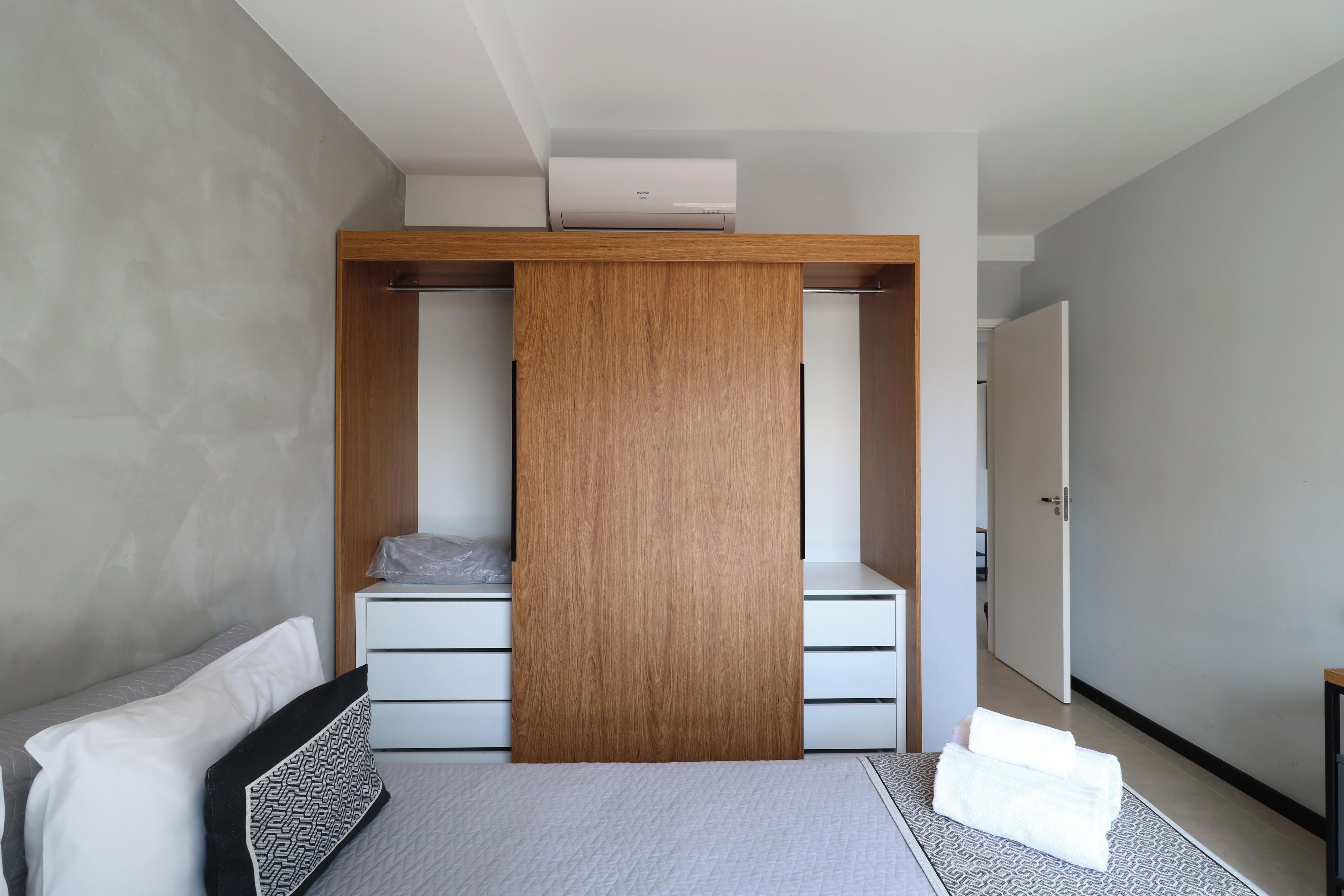 A modern bedroom with a built-in wardrobe, a bed with a patterned bedspread, and a visible air conditioning unit.