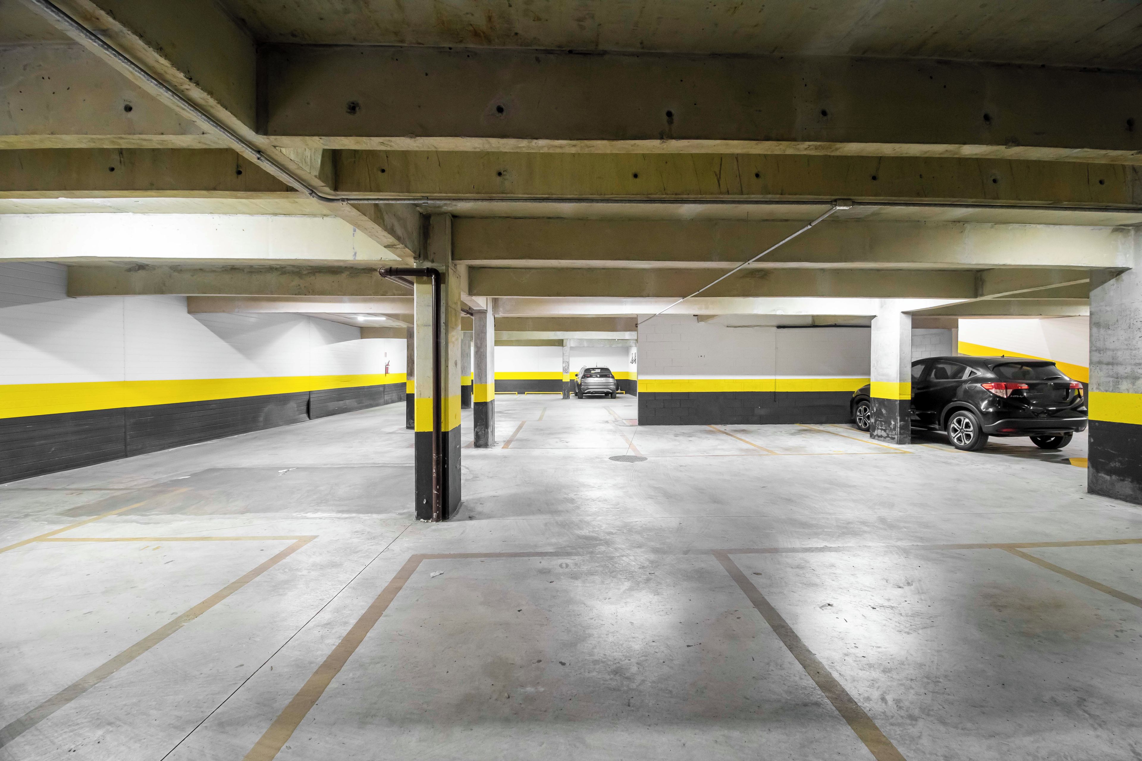An underground parking garage with concrete pillars, yellow and black painted walls, and a few parked cars.