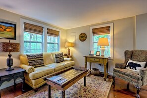 A cozy living room with a leather sofa, a wooden coffee table, and a patterned rug. - Sunny "Charmer" Cottage w/ Folk Art & Country Primitive Style — Sleeps 4 (Lakemont)