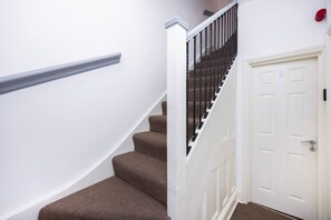 A staircase with a handrail, carpeted steps, and a white door with a number. - Earl`s Court Residence | Elegant Studio | London (Greater London)