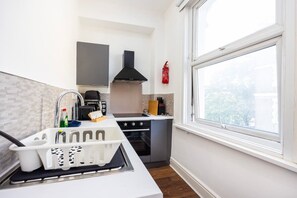 A compact kitchen with a sink, stove, and a window providing a view. - Earl`s Court Residence | Elegant Studio | London (Greater London)