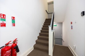 A staircase with fire extinguishers on the wall and a fire exit sign. - Earl`s Court Residence | Elegant Studio | London (Greater London)