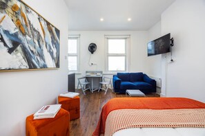 Ein modernes Zimmer mit einem Bett, einem blauen Sofa, einem kleinen Tisch und einem Schreibtisch mit Stuhl.