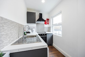 A modern kitchen with a stainless steel sink, a stove, and a window providing a view. - Earl`s Court Residence | Stylish Studio | London (Greater London)