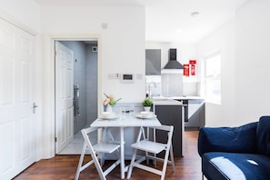Une cuisine moderne avec des meubles blancs, une table à manger avec des chaises et un canapé bleu dans une pièce lumineuse dotée d’une porte et d’une fenêtre.