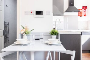 A modern kitchen with a white table set for dining, a built-in oven, and a stove. - Earl`s Court Residence | Stylish Studio | London (Greater London)