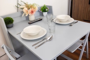 A dining table set with plates, bowls, cutlery, a glass, and a remote control. - Earl`s Court Residence | Stylish Studio | London (Greater London)