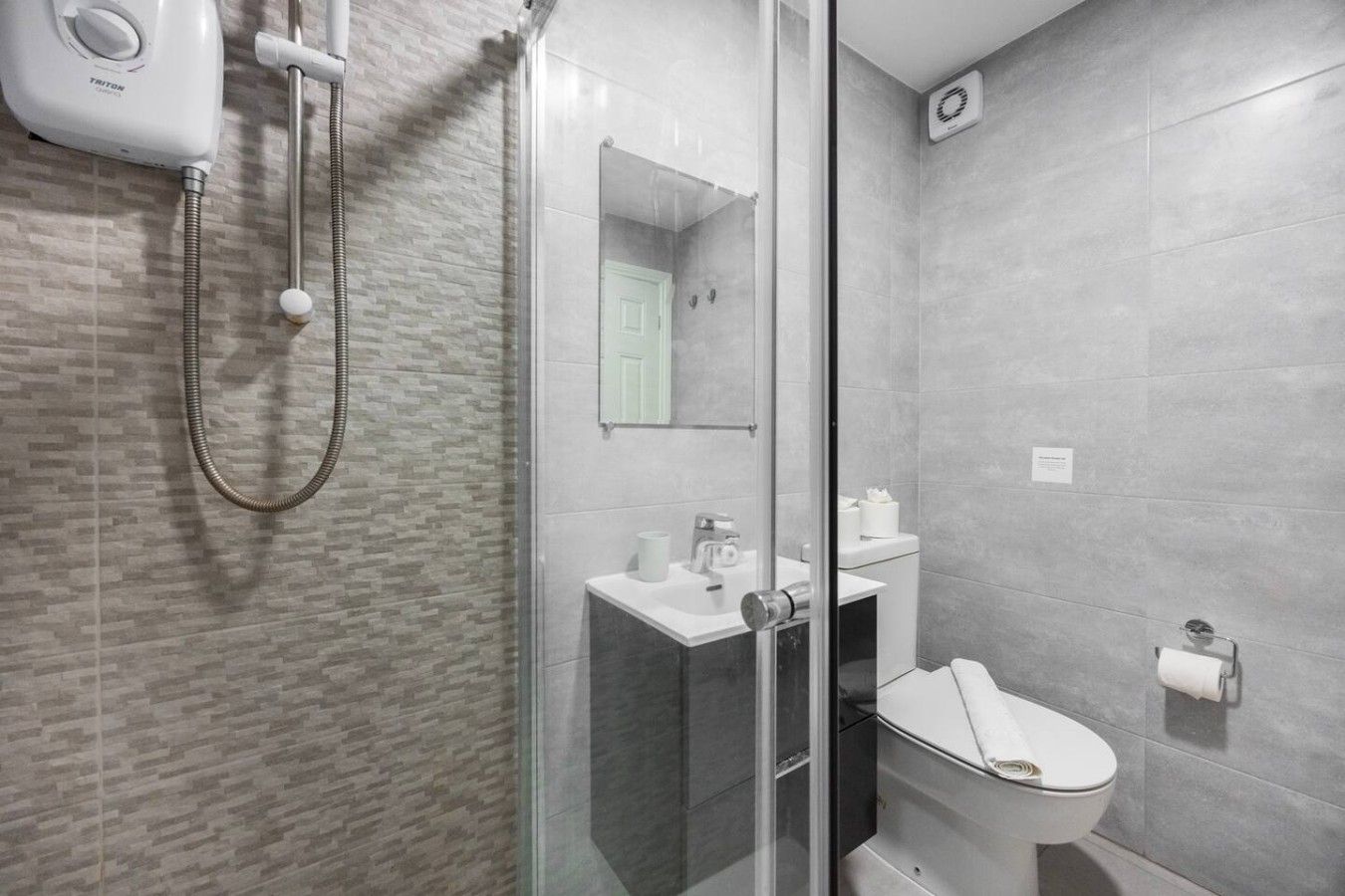 Een moderne badkamer met een douchecabine van glas, een toilet en een wastafel met een spiegel erboven.