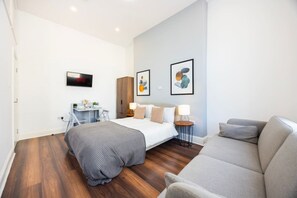 A modern hotel room with a bed, a desk, a sofa, and artwork on the walls. - Earl`s Court Residence | Stylish Studio | London (Greater London)