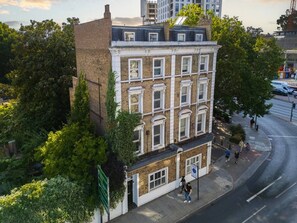 A multi-story building with a brick facade, large windows, and a corner location with a sidewalk. - Earl`s Court Residence | Elegant Studio | London (Greater London)