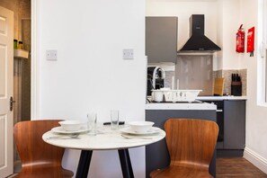 A modern kitchen with a central island, a dining table with chairs, and a white wall with a fire extinguisher. - Earl`s Court Residence | Elegant Studio | London (Greater London)