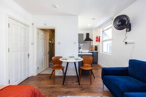 A compact living space with a dining area, a kitchenette, and a blue sofa. - Earl`s Court Residence | Elegant Studio | London (Greater London)