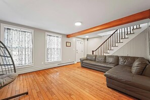 Un salon spacieux doté d’un parquet, d’un canapé en cuir, d’un fauteuil à bascule et d’un escalier avec des rampes en bois.