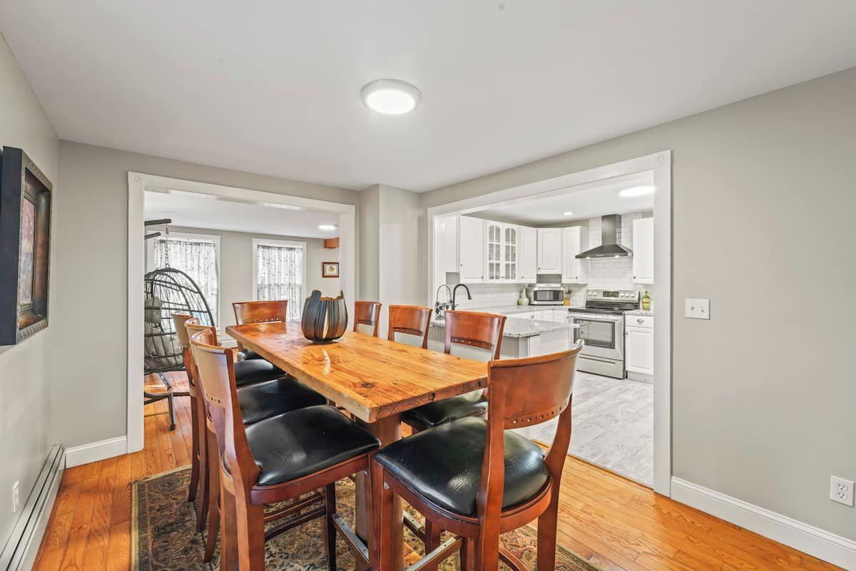A dining area with a wooden table and chairs, a kitchen in the background, and a view of the living room.