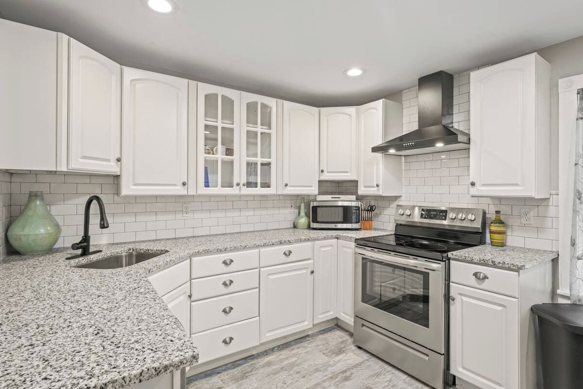 A kitchen with white cabinetry, a granite countertop, a stainless steel stove, and a microwave.