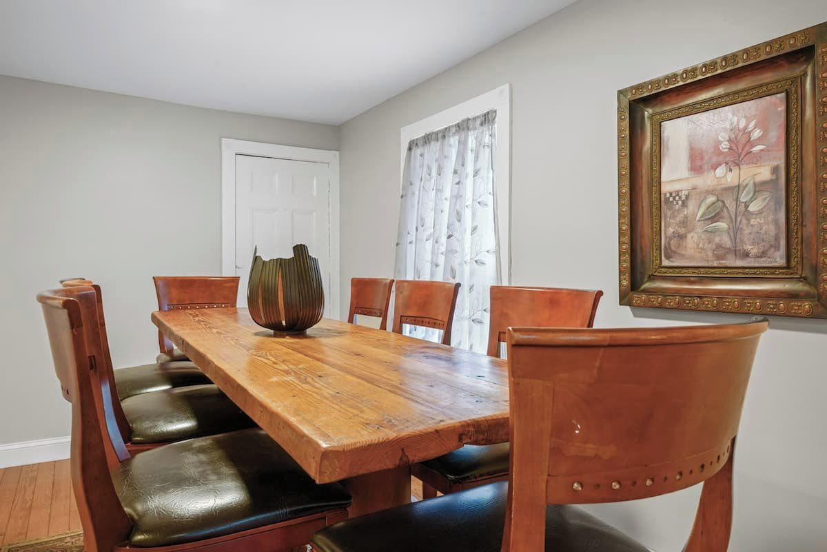 A dining room with a wooden table and leather chairs, a vase, and a framed picture on the wall.