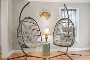 Deux fauteuils suspendus avec coussins, une petite table avec une lampe et un élément décoratif mural.