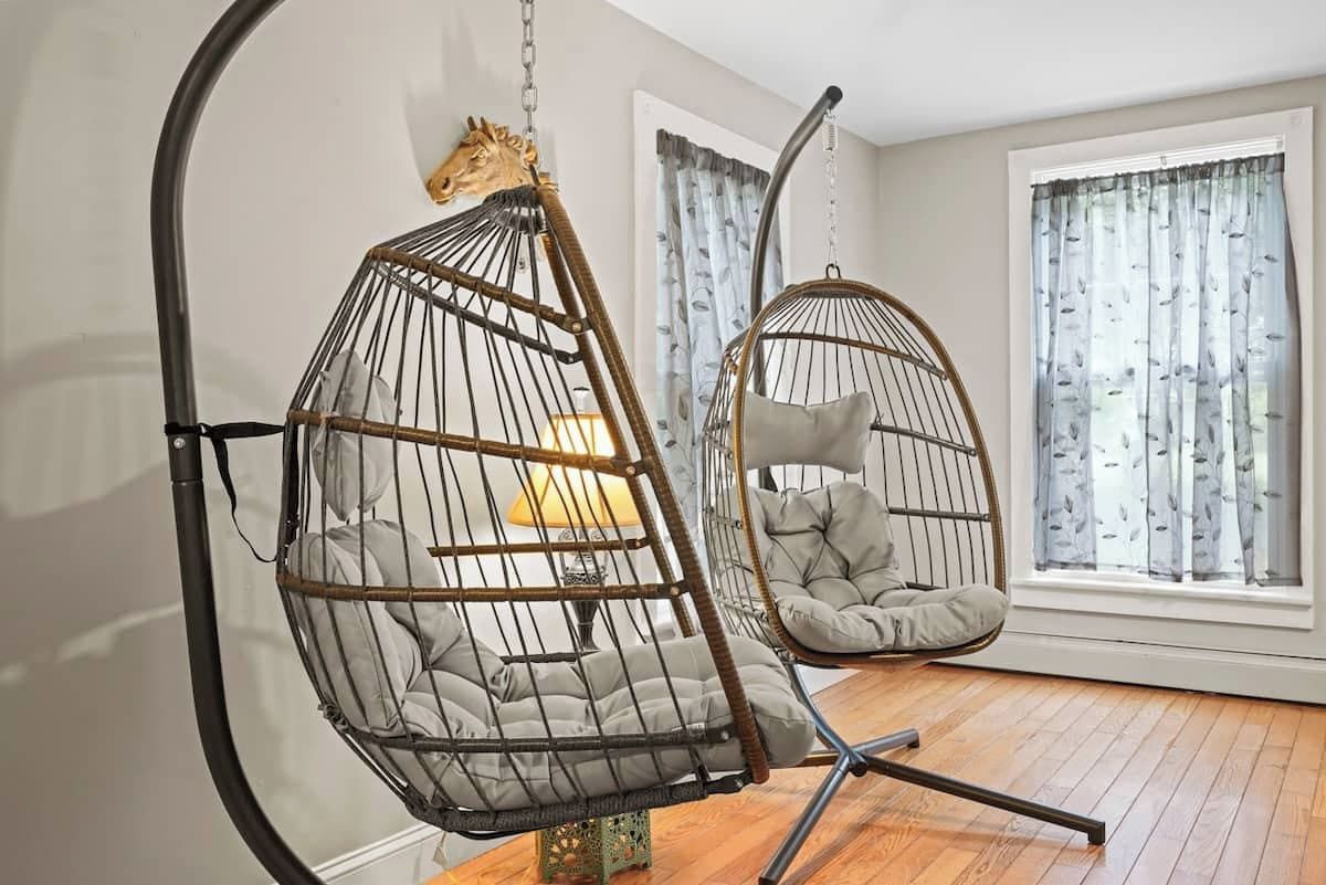 A room with a hanging chair and a cushioned chair near a window with curtains.