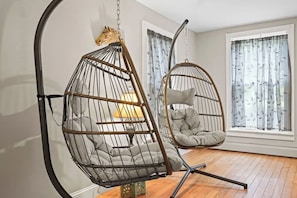 A room with a hanging chair and a cushioned chair near a window with curtains. - Walk to Saratoga Track | 2 Kings | Pet OK (Saratoga Springs)