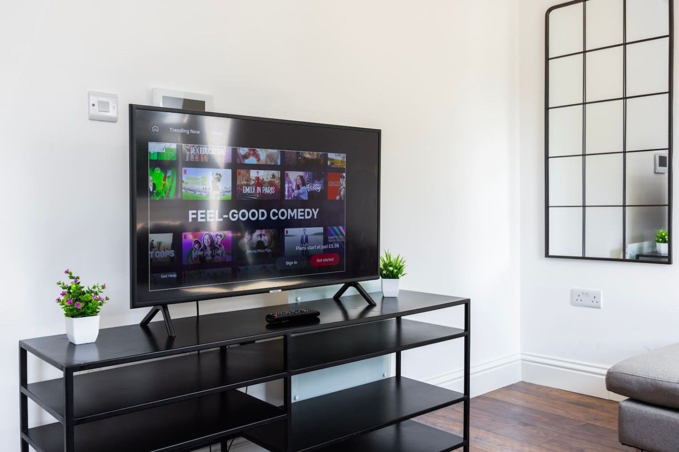 A flat-screen TV on a black stand with a streaming service interface displaying various shows and movies.