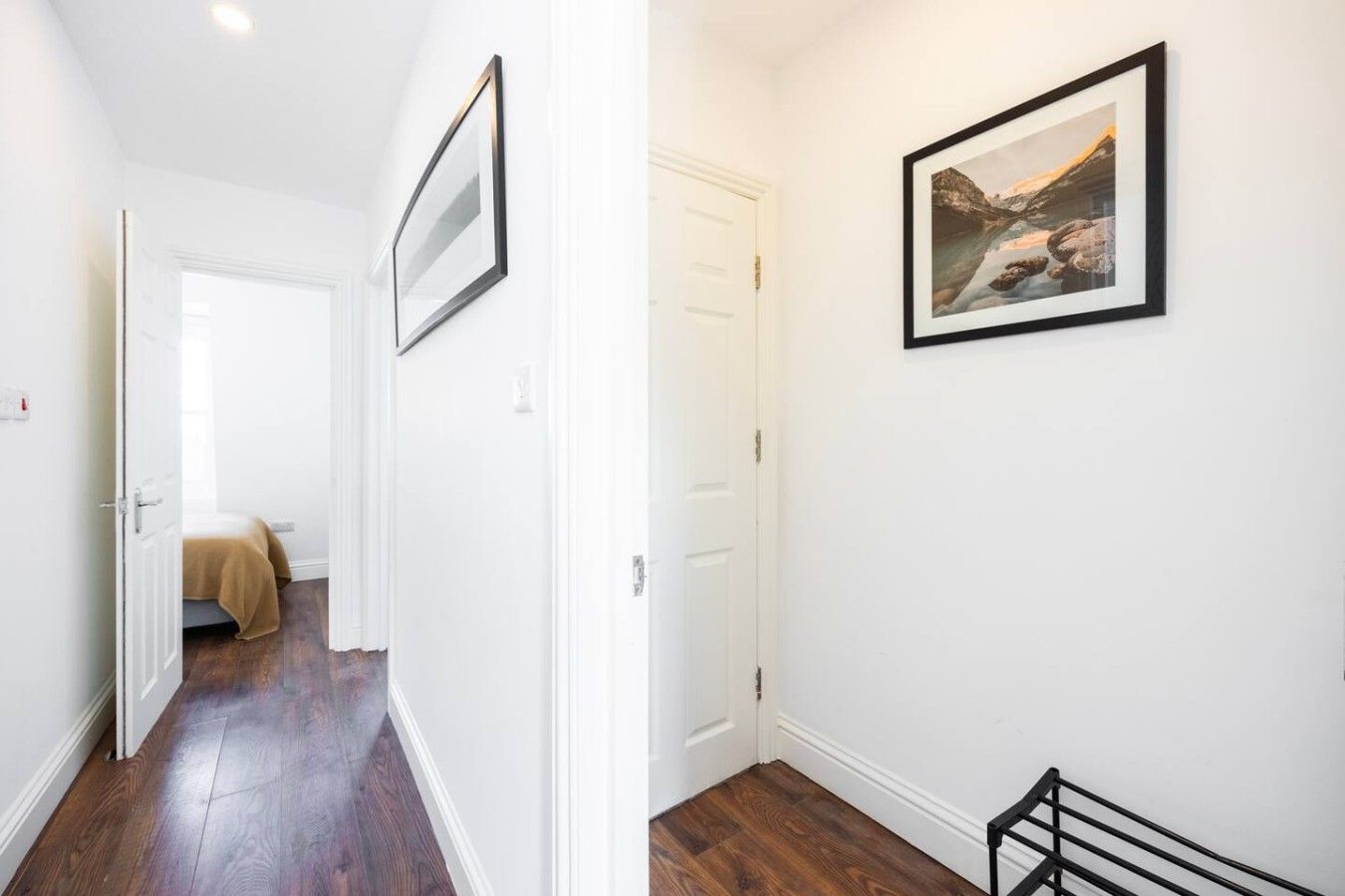 A hallway with a wooden floor, white walls, and a framed picture on the wall.