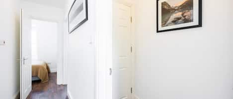 A hallway with a wooden floor, white walls, and a framed picture on the wall.